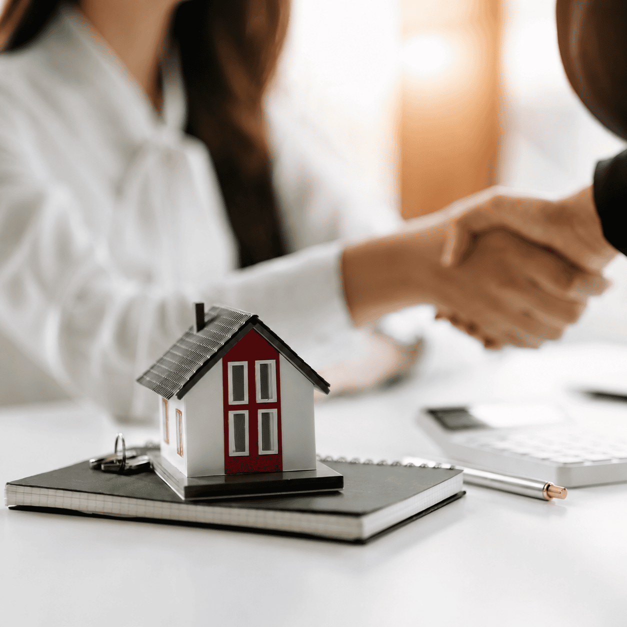 Acuerdo inmobiliario representado por un apretón de manos y una maqueta de vivienda.